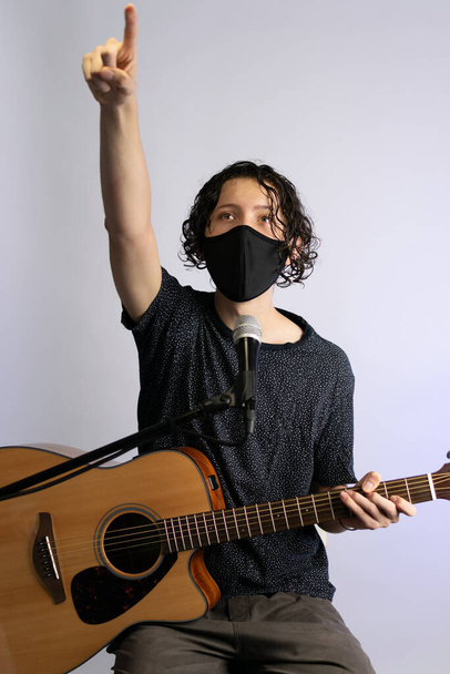Müzisyen, 2020 salgın ve sosyal mesafe ölçümleri nedeniyle siyah bir maske takarak akustik gitar çalıyor - Fotoğraf, Görsel