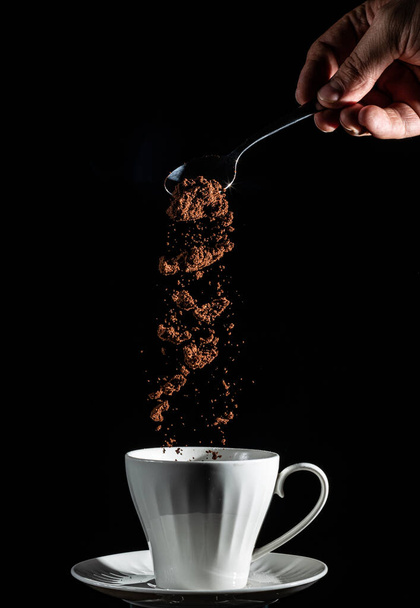 Teaspoon of fresh grounded coffee being pour into the white porcelain cup from high point. Low key, black isolated background. - Foto, Imagem