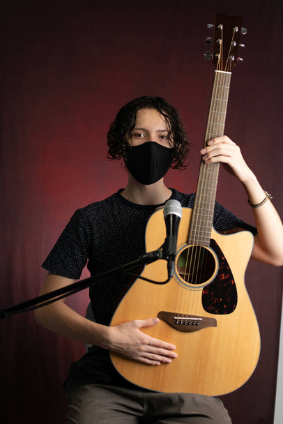 Músico toca guitarra acústica con mascarilla facial debido a las medidas pandémicas y de distanciamiento social de 2020 - Foto, Imagen