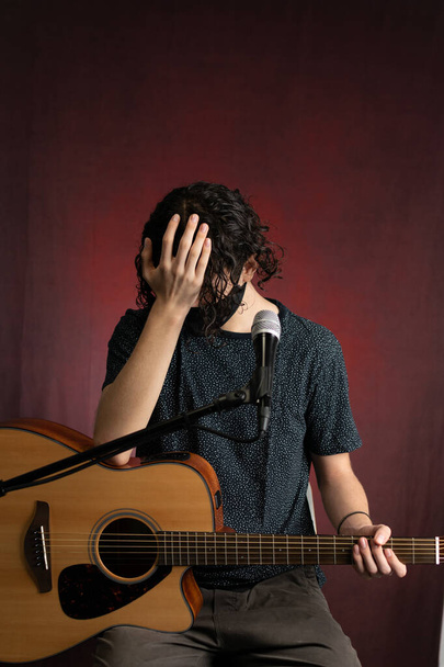 Músico toca guitarra acústica usando uma máscara facial devido a 2020 pandemia e medidas de distanciamento social - Foto, Imagem