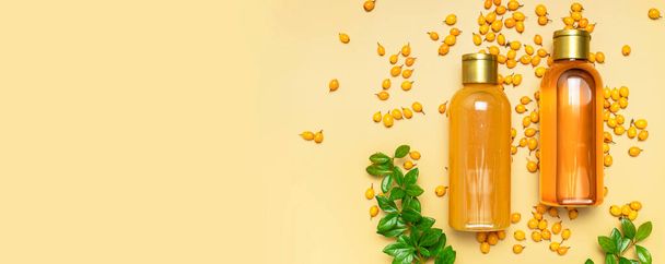Natural beauty product concept. Cosmetic bottle containers, sea buckthorn berries, green barberry leaves on beige background flat lay top view. Blank label for branding mock-up. Beauty and health. - Photo, Image