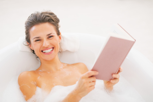 Hymyilevä nuori nainen lukee kirjaa kylpyammeessa
 - Valokuva, kuva