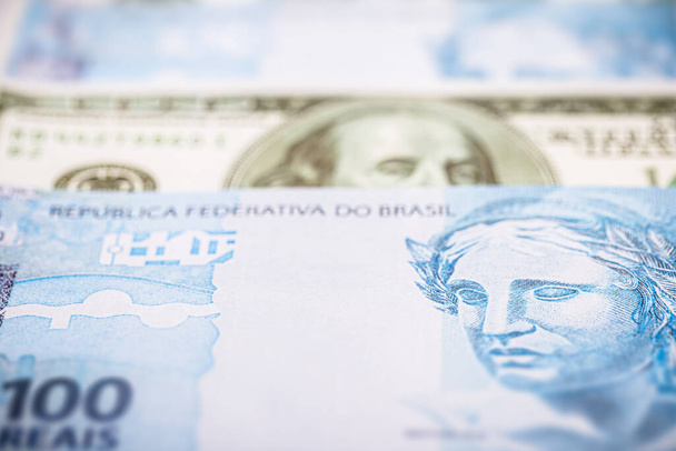 egy 100 reais-es brazil bankjegy részletei, 100 amerikai dollár bankjegyei közé zárva. Gazdasági válság és magas amerikai valuta - Fotó, kép