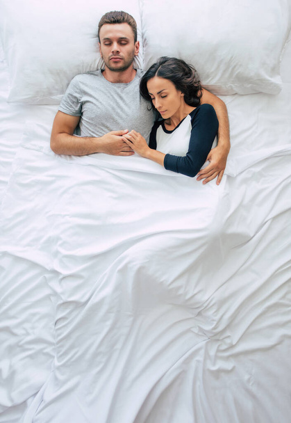 Bedtime. The family are sleeping. Beautiful young couple in love are lying on the big white bed and resting. Husband and wife together in bed. Top view photo - Zdjęcie, obraz