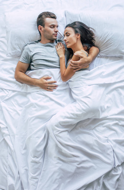 Bedtime. The family are sleeping. Beautiful young couple in love are lying on the big white bed and resting. Husband and wife together in bed. Top view photo - Foto, Bild