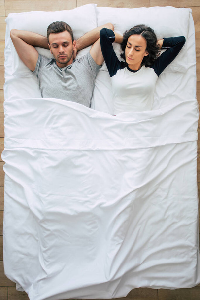 Bedtime. The family are sleeping. Beautiful young couple in love are lying on the big white bed and resting. Husband and wife together in bed. Top view photo - Fotó, kép
