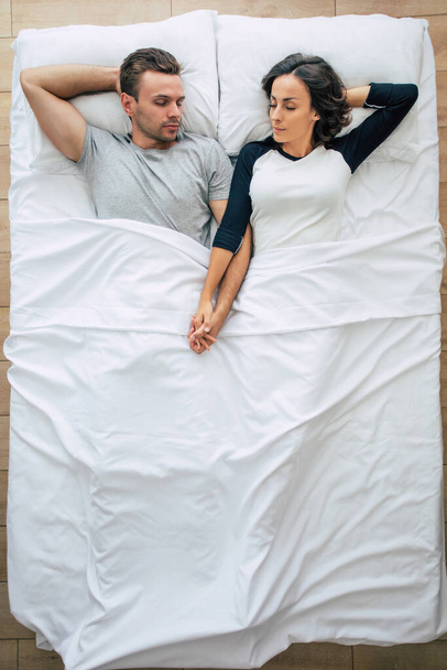 Bedtime. The family are sleeping. Beautiful young couple in love are lying on the big white bed and resting. Husband and wife together in bed. Top view photo - Fotografie, Obrázek