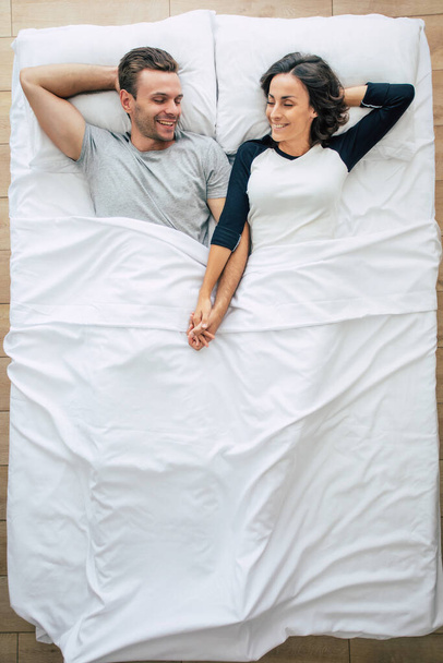 Bedtime. The family are sleeping. Beautiful young couple in love are lying on the big white bed and resting. Husband and wife together in bed. Top view photo - Fotoğraf, Görsel