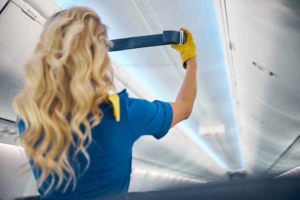 Очаровательная стюардесса в желтых перчатках, работающая в самолете с оборудованием для безопасности на борту - Фото, изображение