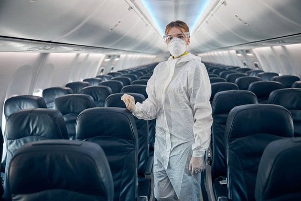 Flugbegleiterin steht mit Schutzbrille im Salon des Zivilflugzeugs - Foto, Bild