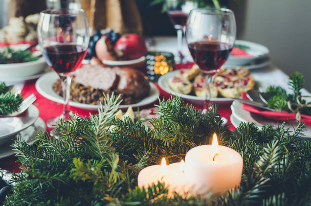 Family together Christmas celebration concept. Festive place setting for holiday dinner with natural decorations from fir tree branches. Lightning candles on foreground, served table on background. - Foto, Imagem