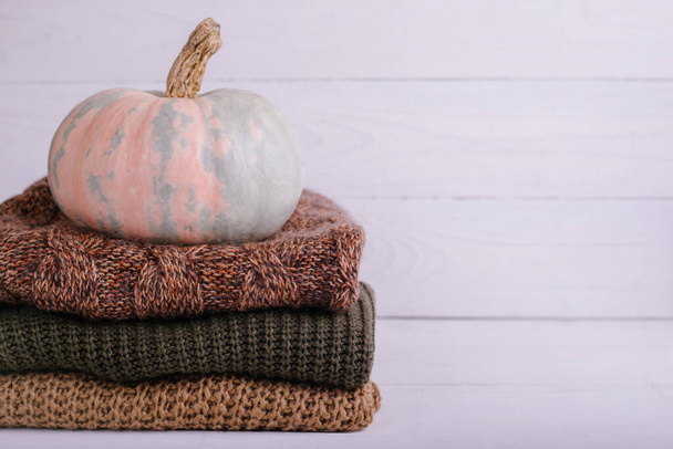 A pile of warm knitted sweaters on white wooden background with pumpkin, knitwear, place for text, Autumn sale concept. Copy Space. - Photo, Image