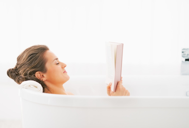 Young woman reading book in bathtub - Foto, Bild