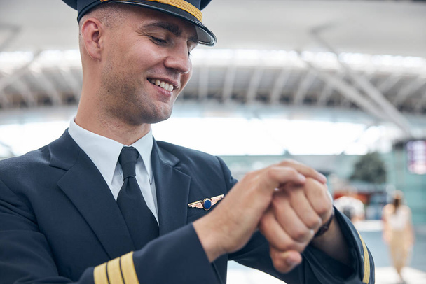 Веселий пілот чоловічої статі дивиться на наручний годинник і посміхається
 - Фото, зображення