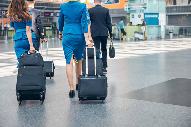 Члены экипажа, перевозящие чемоданы в терминале аэропорта - Фото, изображение