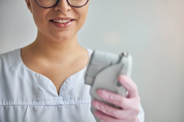 Une femme cosmétologue souriante tient un appareil laser - Photo, image