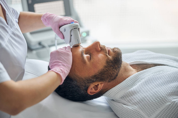 Врач-косметолог лечит мужскую кожу лазерным прибором - Фото, изображение