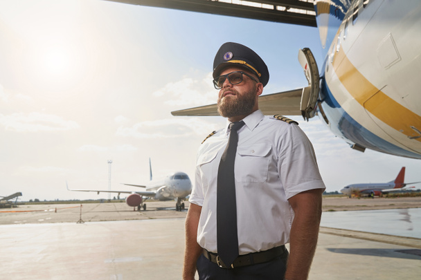 Fiducioso pilota in posa accanto all'aereo in aeroporto - Foto, immagini