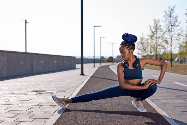 athlete afro woman stretching hamstring leg muscles during outdoor running workout - Foto, imagen