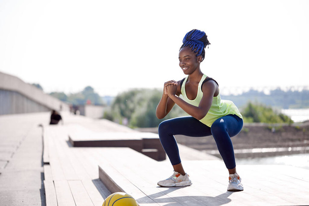 strong sporty black woman doing squat exercises outdoors on fresh air - Foto, immagini