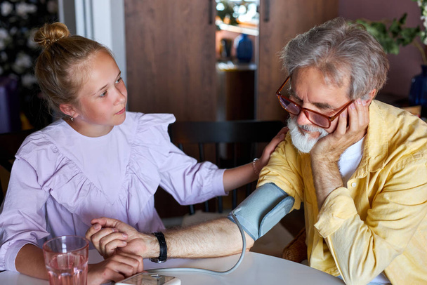 little child girl take care of sick granddad, measure blood pressure using a tonometer - Fotoğraf, Görsel