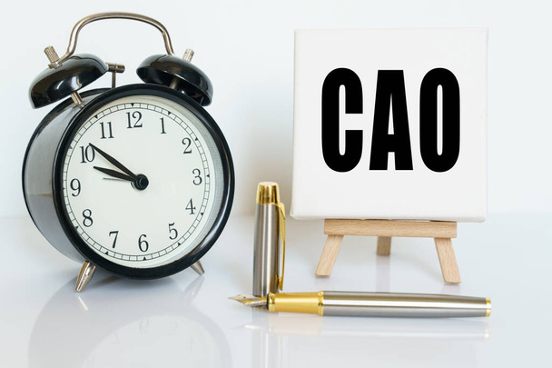 Business and finance concept. On the table there is a clock, a pen and a stand with a card on which the text is written CAO. CHIEF ACCOUNTING OFFICER - 写真・画像