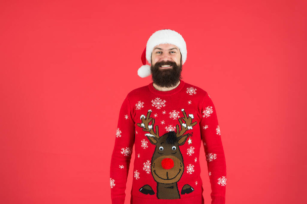 happy new year. cheerful hipster funny knitted sweater. warm clothes in cold winter weather. holiday season mood. bearded man santa hat red background. merry christmas. ready for xmas party - Photo, image