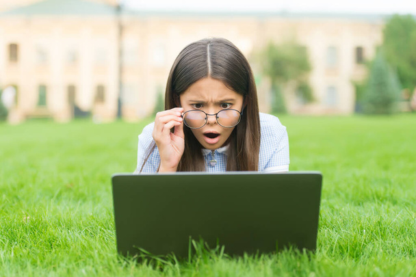 Nee, hoor. terug naar school. tiener meisje gebruik computer op groen gras in het park. kind met bril en notitieboekje. nieuwe technologie in het moderne leven. Studeren. Verrast kind dat aan laptop werkt. online onderwijs - Foto, afbeelding