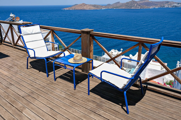 İki beyaz sandalyesi, masası ve deniz manzaralı ahşap bir villa ya da otel terası. - Fotoğraf, Görsel