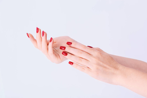 Hands of a young woman with long red manicure on nails against white background - Photo, Image