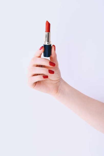 Woman hand with long red manicure on nails holding red lipstick on white background - Фото, зображення