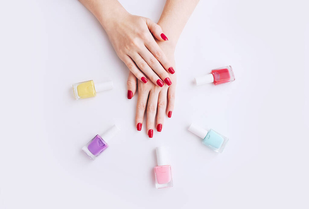 Smalto. Manicure d'arte. Bottiglie di smalto multicolore intorno alle mani femminili con eleganti unghie rosse - Foto, immagini