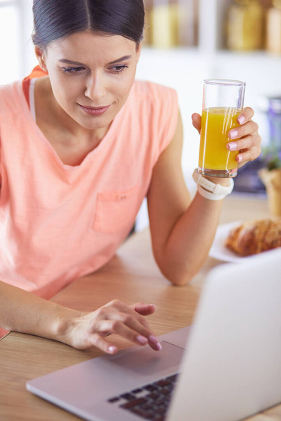 Молодая женщина на кухне с ноутбуком компьютер ищет рецепты, улыбаясь. Концепция пищевого блогера - Фото, изображение