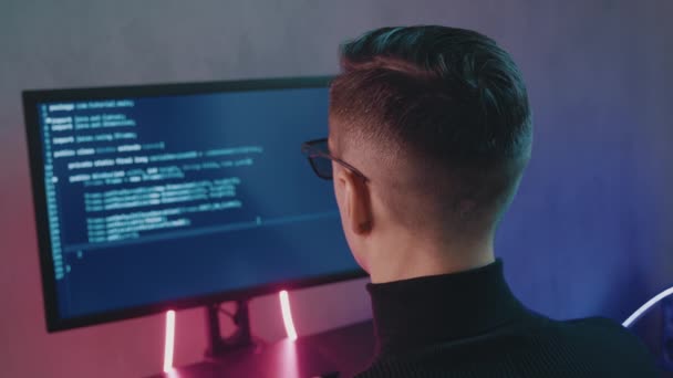 ネオンライトで屋内ネットワークセキュリティソフトウェアをコーディング男プログラマーの後方ビュー。ハッカーは夜暗いオフィスでコンピュータ画面上のコードを入力します - 映像、動画