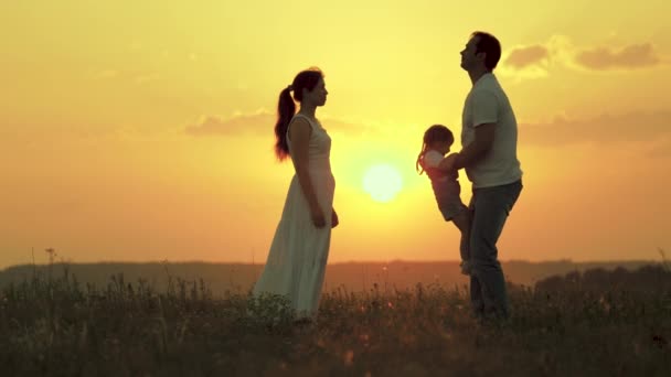 幸せな家族は新鮮な空気の中を歩く。父親は娘と遊んで子供を空中に投げ入れるのを喜んで幸せな母親は家族を賞賛する。ママパパと赤ちゃん家族は畑の夕日に休んでる. - 映像、動画