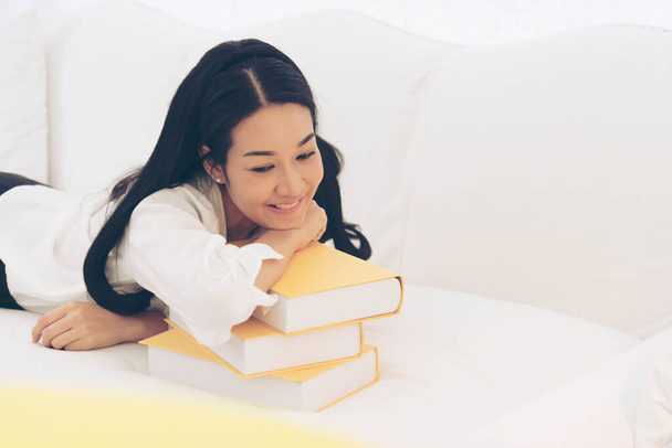 Young Asian Woman student university holding text book on her hands sitting on sofa with colorful pillow. Study hard to get a better grade. Education Concept - Foto, Imagen