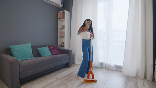 Fiatal pozitív kaukázusi nő viccesen táncol, miközben takarítja a házat - Felvétel, videó