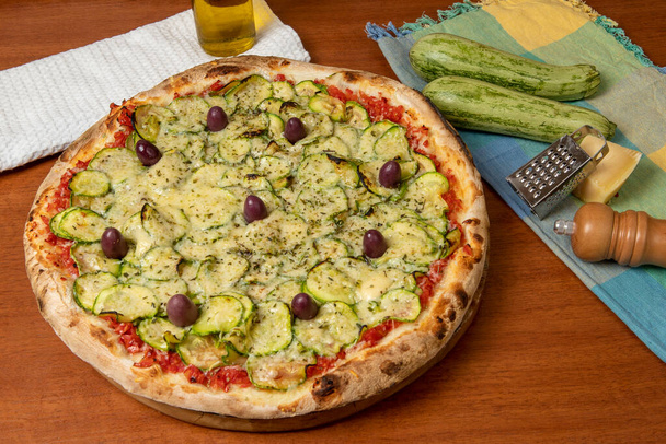 Ízletes olasz vegetáriánus pizza paradicsomszósszal, paprikával, olívabogyóval és cukkinivel, fa asztali háttérrel. portugál nyelvű szöveg: nyugalom - Fotó, kép