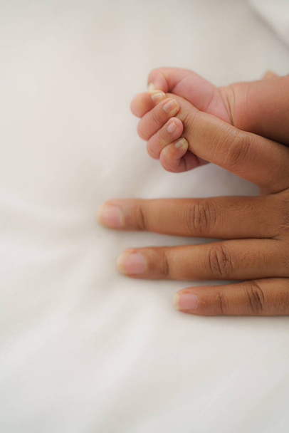 infant baby hand holding mom finger on white bed. - 写真・画像
