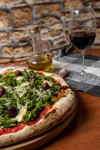 Pizza of broccoli, gorgonzola cheese, black olives, garlic and tomato sauce on wooden table - Photo, Image