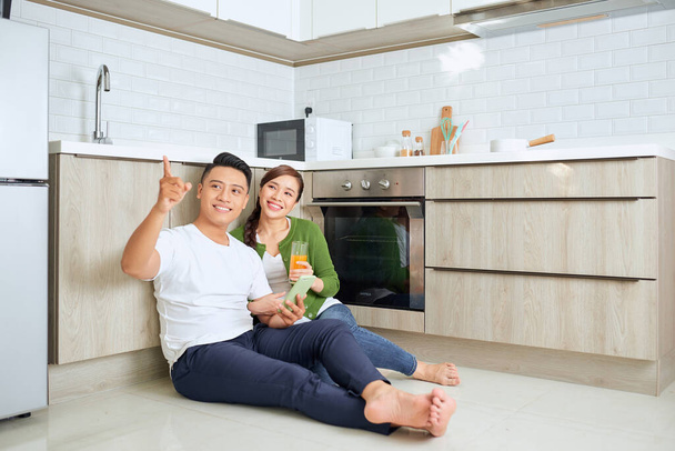 Heureux jeune homme et femme assis sur le sol de la cuisine et prendre un café. Jeune couple assis sur le sol de la cuisine et souriant. - Photo, image