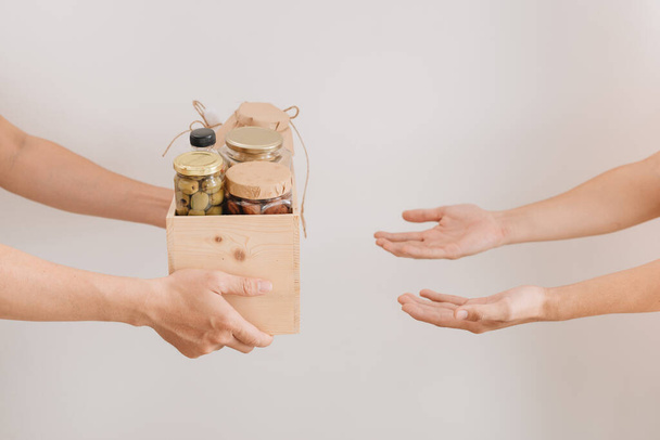 Skrzynka darowizn z różnymi pokarmami. Wolontariuszka podaje kartonowe pudełko z suchymi płatkami zbożowymi, puszkami, jajkami, olejem. Z ręki na rękę.  - Zdjęcie, obraz