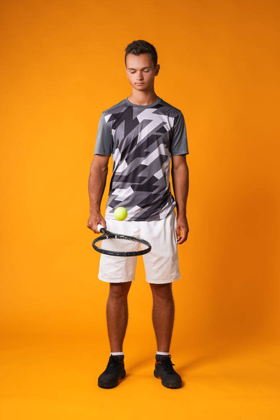 Full-length portrait of a tennis player man in action against orange background - Фото, зображення