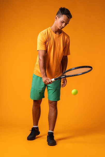 Full-length portrait of a tennis player man in action against orange background - 写真・画像
