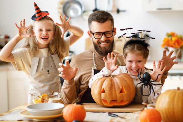 Бородатый мужчина и девочки с Джеком о фонарь улыбаясь и жестикулируя, пугая камеру во время празднования Хэллоуина на кухне в доме - Фото, изображение