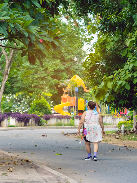 Widok z tyłu Azjatki starsza kobieta nosi słuchawki do słuchania piosenki spaceru i jogging dla dobrego zdrowia w parku publicznym.Senior jogger w przyrodzie. Starsza kobieta ciesząca się spokojną naturą.Koncepcja opieki zdrowotnej - Zdjęcie, obraz