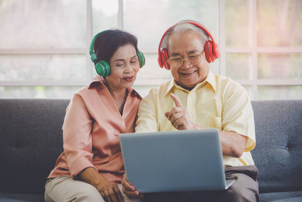 Heureux couple de personnes âgées est watiching et écouter du film de musique à partir d'un ordinateur portable avec casque coloré. - Photo, image