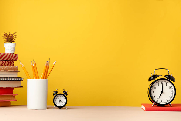 Cup of pencils and notepads on desk against yellow background - Foto, immagini