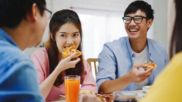 Χαρούμενοι νεαροί φίλοι τρώνε στο σπίτι. Ασιατικό οικογενειακό πάρτι τρώγοντας πίτσα και γελώντας απολαμβάνοντας το γεύμα, ενώ κάθονται στο τραπέζι μαζί στο σπίτι. Εορτασμός διακοπών και ομαδικότητας. - Φωτογραφία, εικόνα