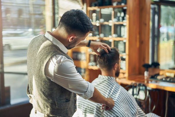 Focused barber looking carefully at the hair of his client - Φωτογραφία, εικόνα